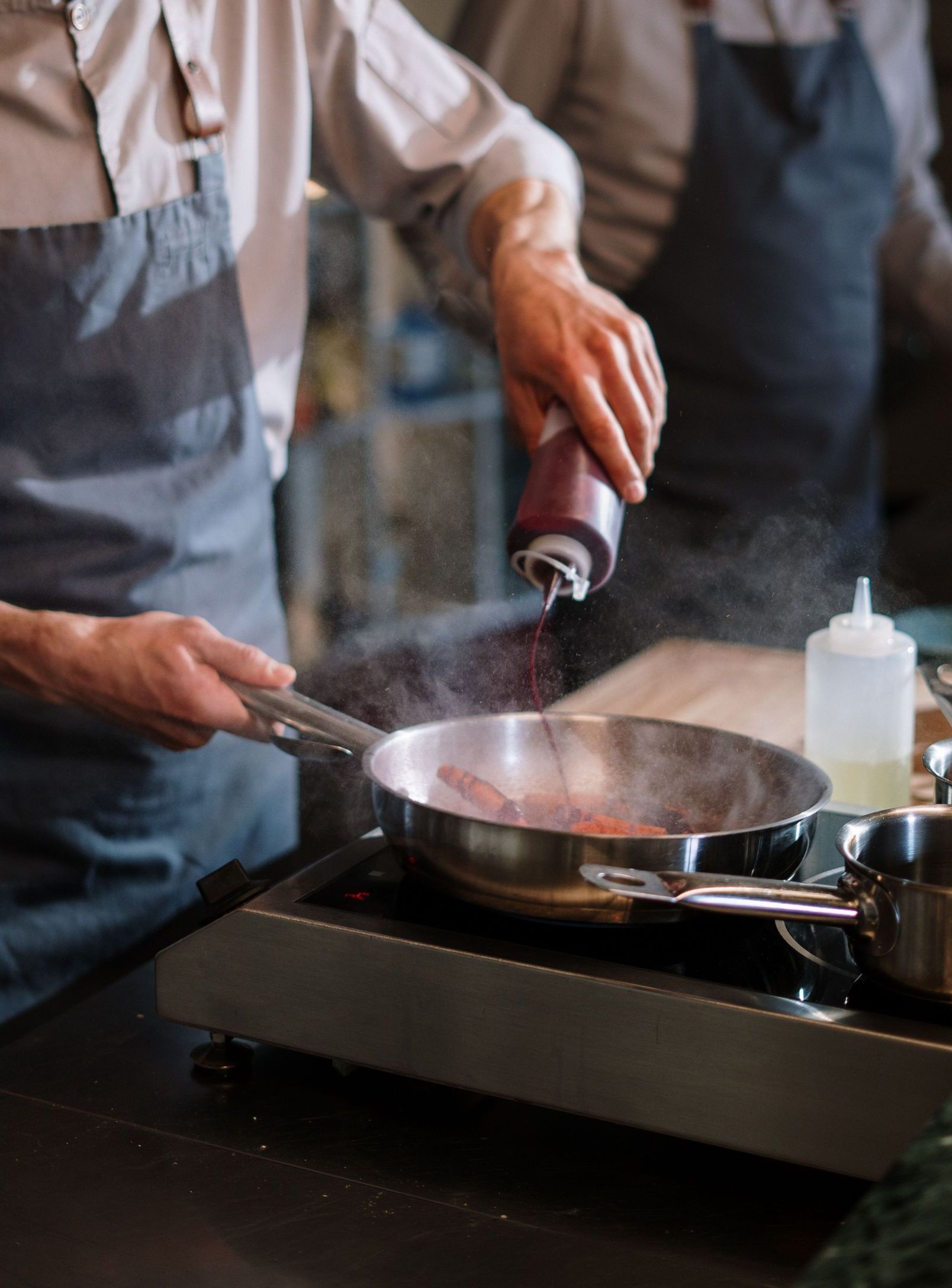 Two chefs in aprons work together in a modern kitchen, preparing food with focus and skill.