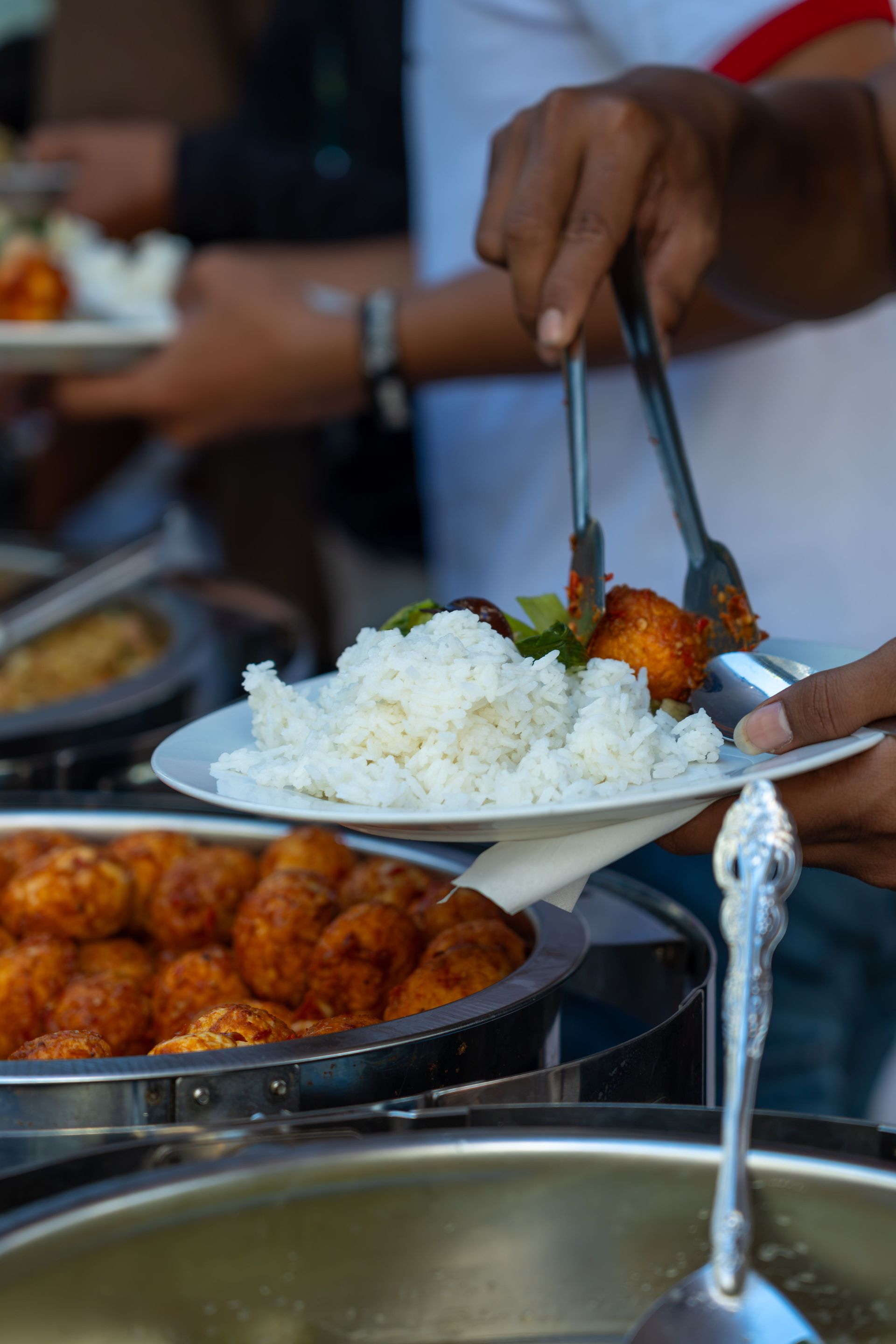 A buffet plate with rice and meatballs being served by a person with tongs at an outdoor event.